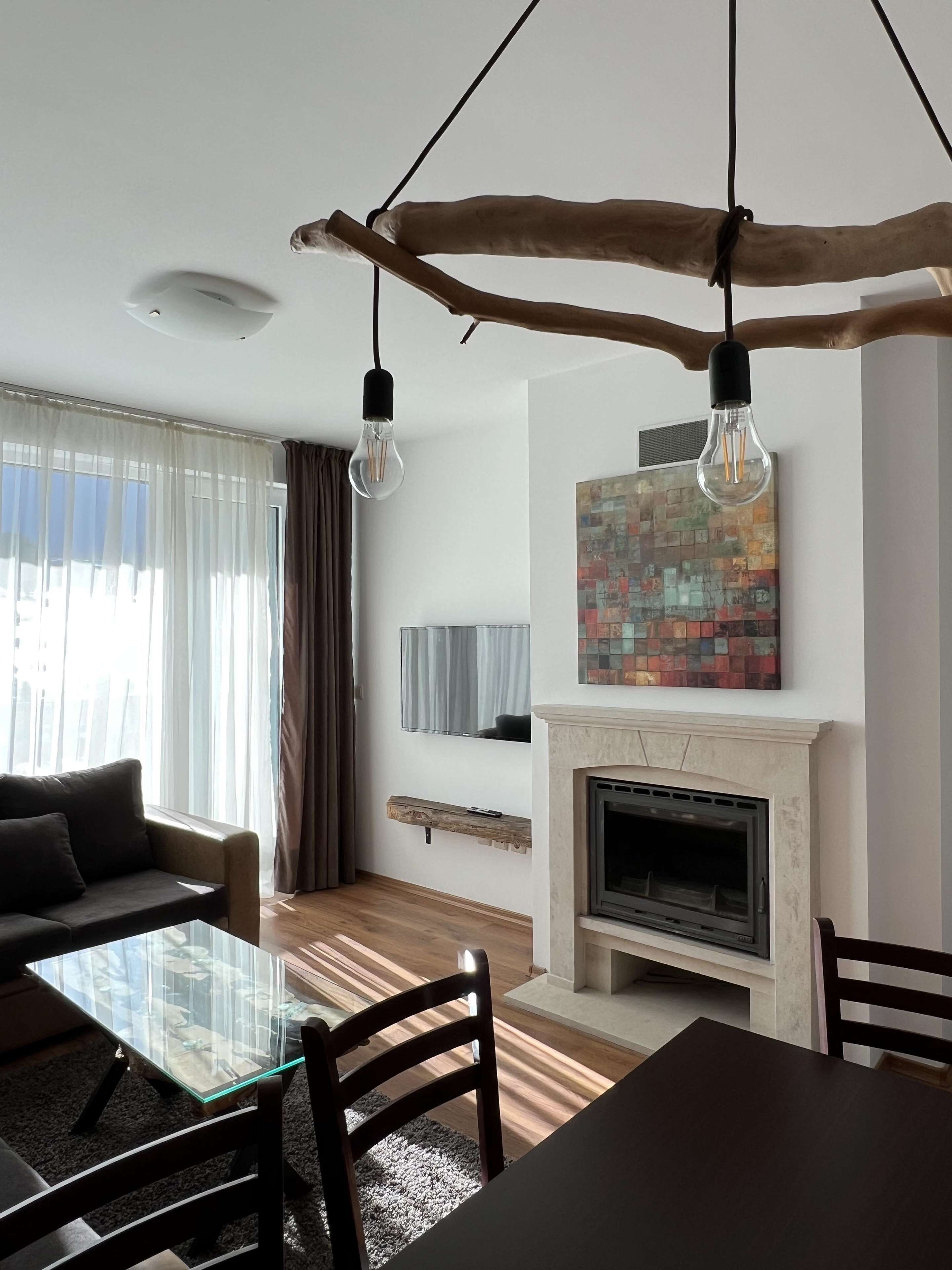 Una sala de estar moderna con una mesa de centro de vidrio, sillas de madera oscura, una chimenea y un televisor montado.