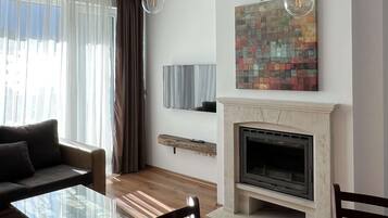 Una sala de estar moderna con una mesa de centro de vidrio, sillas de madera oscura, una chimenea y un televisor montado.