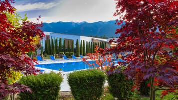 Un edificio moderno con piscina, rodeado de árboles de hojas rojas y montañas al fondo.