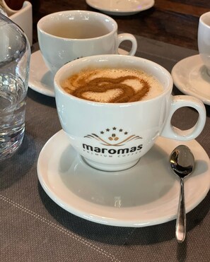 A cup of coffee with latte art on a saucer labeled "Maromas Premium Coffee."