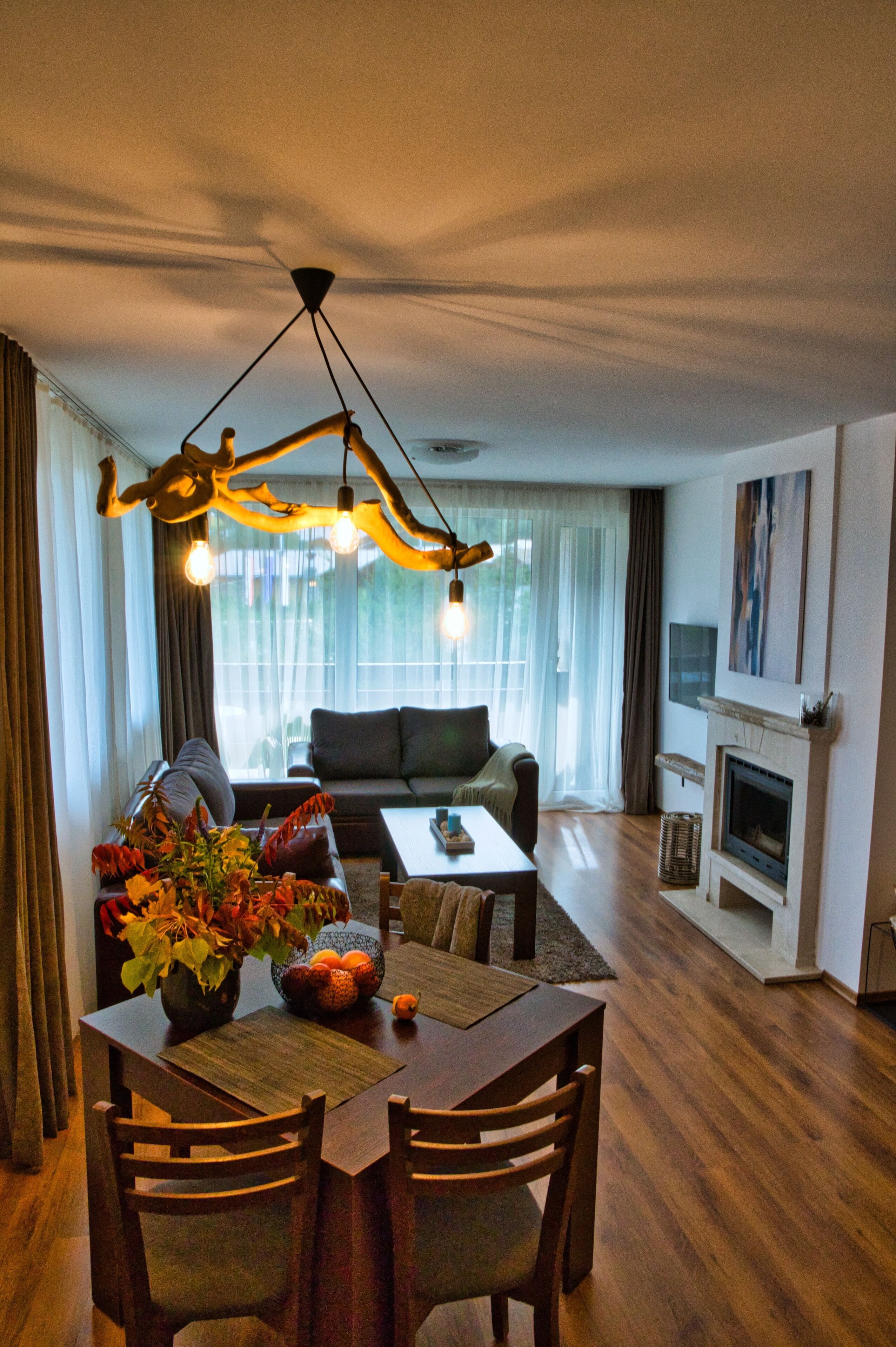 Una sala de estar moderna con comedor, chimenea y un amplio ventanal con cortinas.