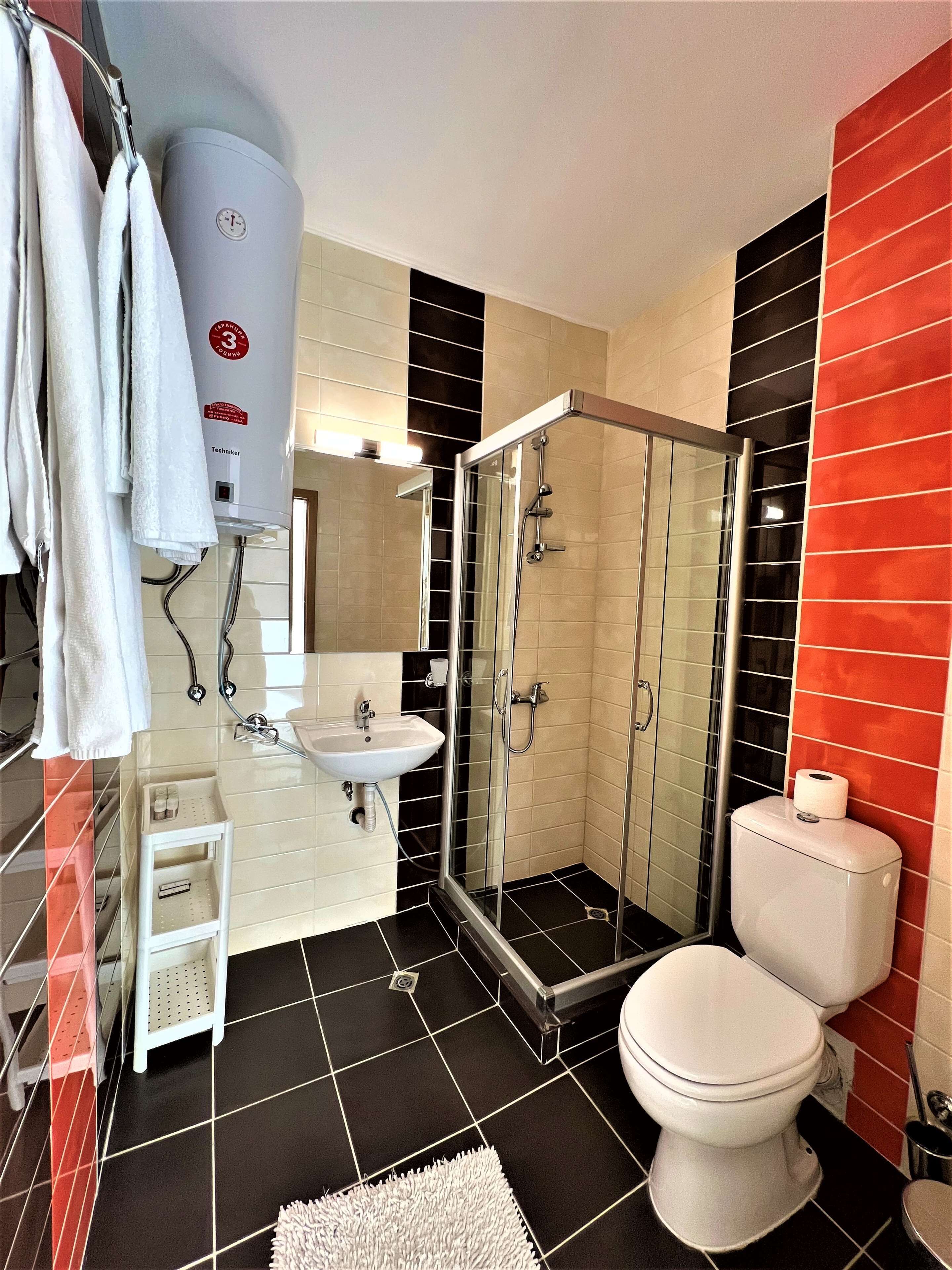 Un bany modern amb dutxa tancada amb vidre, vàter blanc i un lavabo amb mirall a sobre.