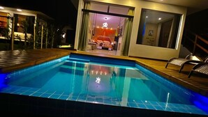 A swimming pool with a wooden deck, a glass door entrance, and a view of the interior.