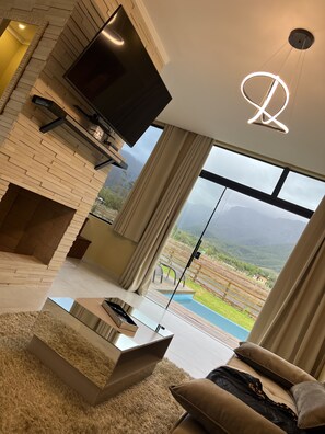 A modern living room with a flat-screen TV, a fireplace, a glass coffee table, and a sofa. - Pousada Green Canyons (Praia Grande)
