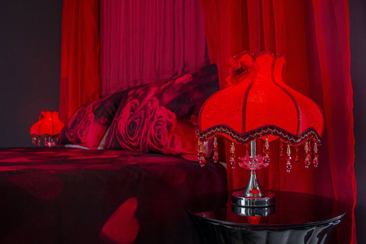 Une pièce avec un lit, une lampe rouge et un rideau rouge.
