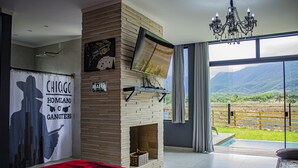 A modern bedroom with a fireplace, a large TV, and a view of a vineyard through the sliding glass door.