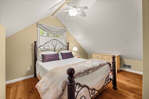 A bedroom with a sloped ceiling, a bed with a headboard, a nightstand, a dresser, and a ceiling fan. - Crane Cove: 4 bedroom Lake Home on Keuka Lake (Penn Yan)
