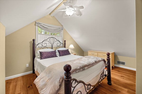 A bedroom with a sloped ceiling, a bed with a headboard, a nightstand, a dresser, and a ceiling fan.