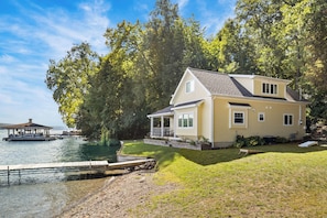 A two-story house with a dock extending into a lake, surrounded by trees.