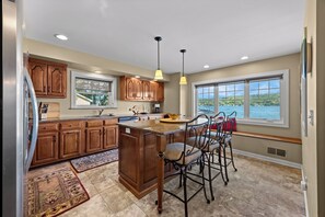 A kitchen with wooden cabinets, a granite countertop, a built-in island with bar stools, and a view of a lake through large windows.