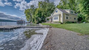 Ett hus med en brygga som sträcker sig ut i en sjö, omgivet av träd och en gräsyta.