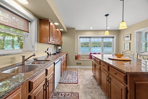 A kitchen with granite countertops, wooden cabinets, a built-in dishwasher, and a view of a lake through large windows. - Crane Cove: 4 bedroom Lake Home on Keuka Lake (Penn Yan)