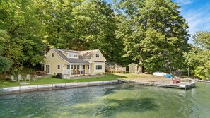 A house with a dock extending into a calm body of water, surrounded by lush greenery. - Crane Cove: 4 bedroom Lake Home on Keuka Lake (Penn Yan)