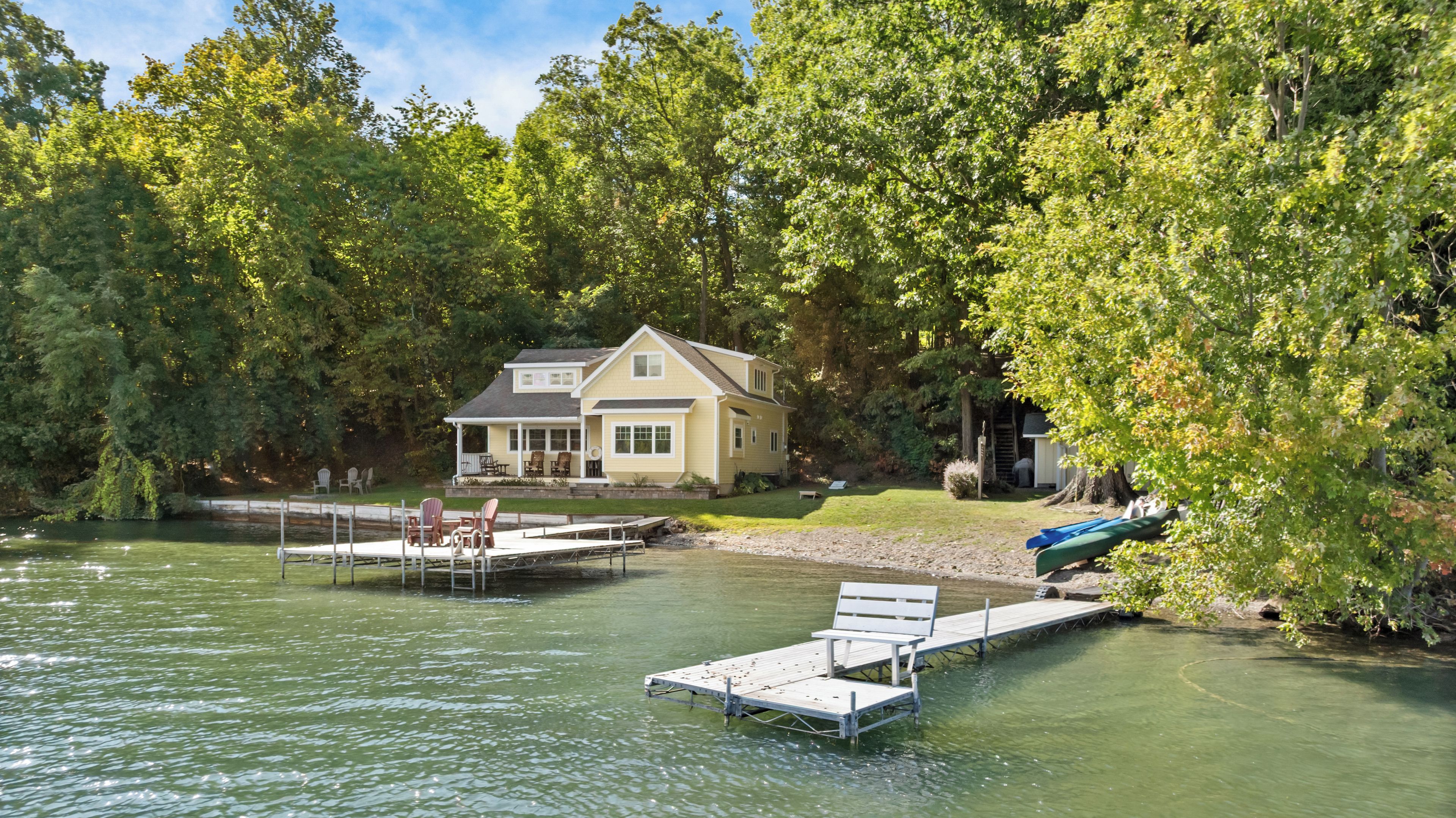 A lakeside property with a dock, chairs, and a house surrounded by trees.
