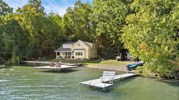 A lakeside property with a dock, chairs, and a house surrounded by trees.