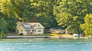 A lakeside property with a main house and a smaller structure, both surrounded by dense trees.