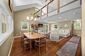 A spacious living area with a high ceiling, wooden dining table, and a cozy seating arrangement.