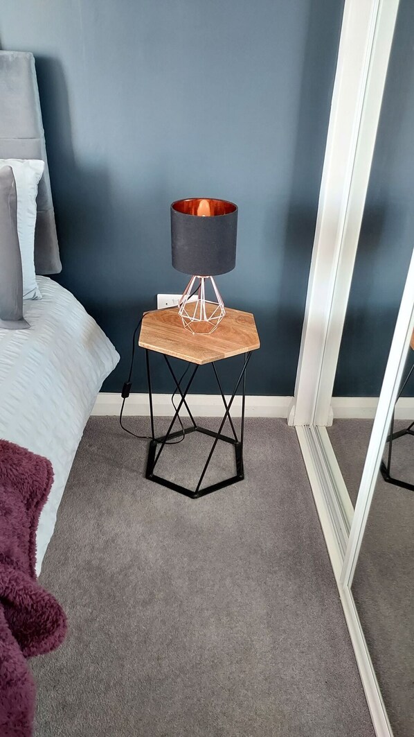 A bedroom with a bed, a nightstand with a lamp, and a mirror.