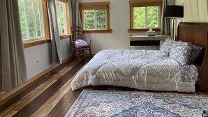A bedroom with a bed, a chair, a desk, and two windows.