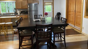 A modern kitchen with wooden cabinets, a stainless steel refrigerator, and a dining area with a large table and chairs.