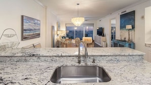A modern kitchen with a large granite countertop, stainless steel sink, and a chandelier. - Gulf Front Luxury-Extra Large Balcony-Regency Isle 907-Signature Properties (Orange Beach)