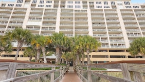 A multi-story hotel with balconies, a wooden walkway, and palm trees. - Gulf Front Luxury-Extra Large Balcony-Regency Isle 907-Signature Properties (Orange Beach)