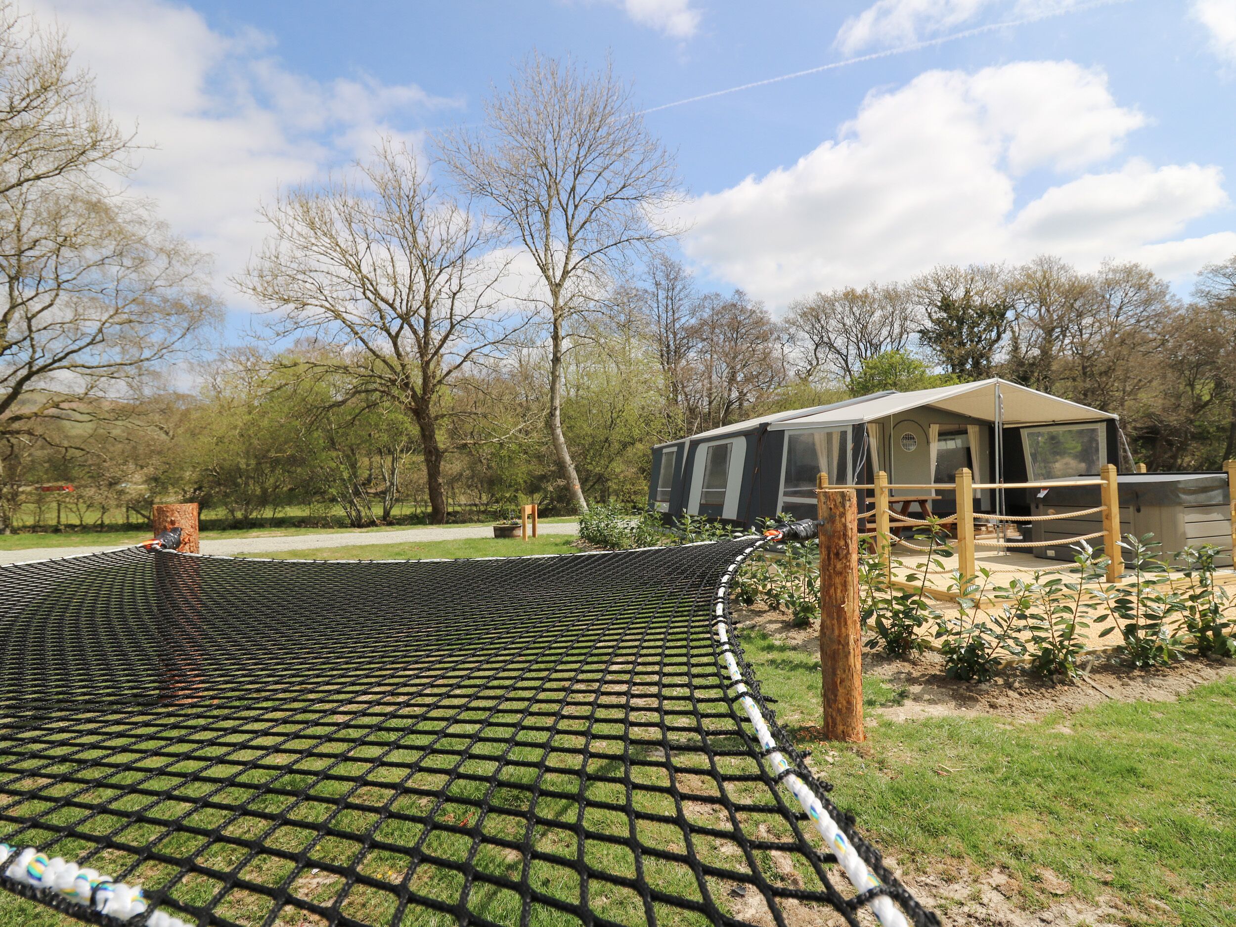 A camping area with a netted enclosure, a covered seating area, and trees in the background.
