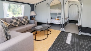 A compact, well-lit room with a sofa, a small round table, a bunk bed, and a lamp.