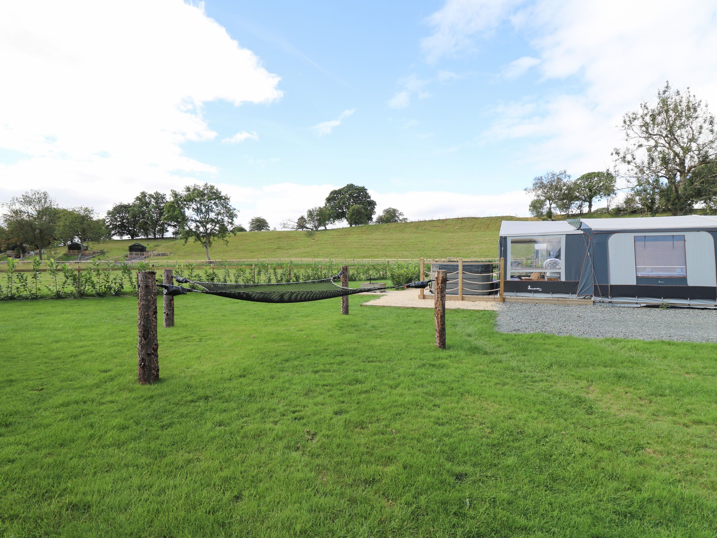 A grassy field with a hammock, a small wooden structure, and a large RV-style accommodation.