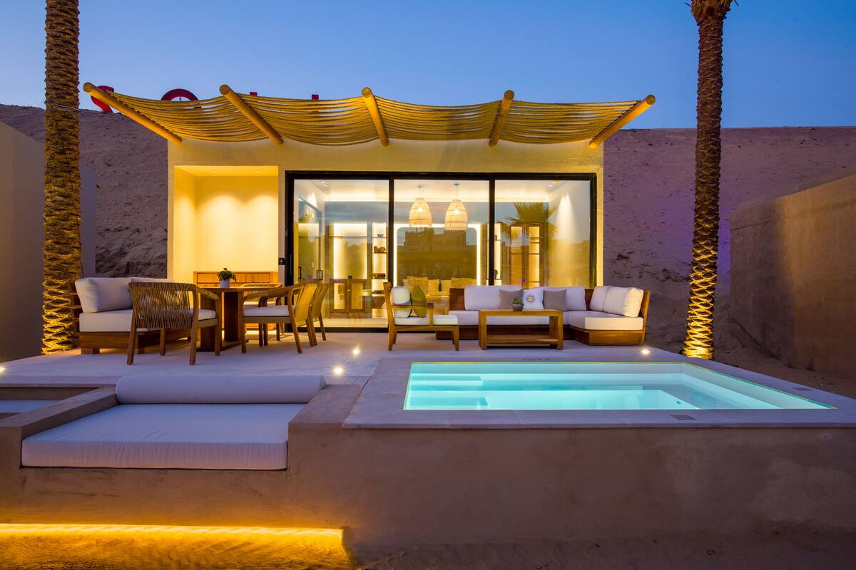 A modern outdoor lounge area with a pool, seating, and a covered patio.