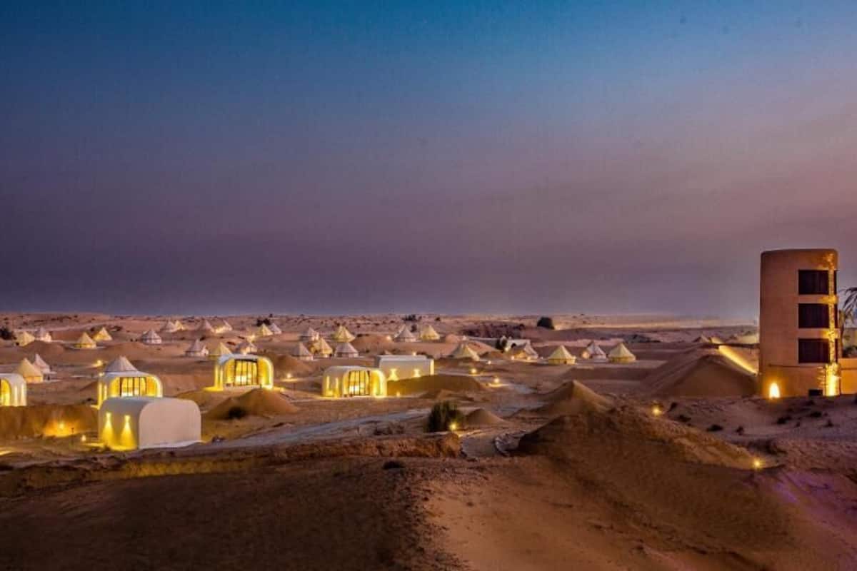A desert resort with multiple dome-shaped tents illuminated at dusk.