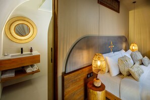 A bedroom with a wooden headboard, a round mirror, a bedside table with a lamp, and a bed with white bedding and decorative pillows.