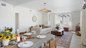 Ein Essbereich mit einem Holztisch, gedeckt für vier Personen, umgeben von Stühlen. Im Hintergrund befinden sich ein Sofa und ein Couchtisch.