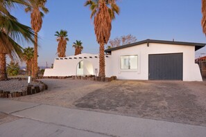 A modern house with a garage, surrounded by palm trees and a clear sky.