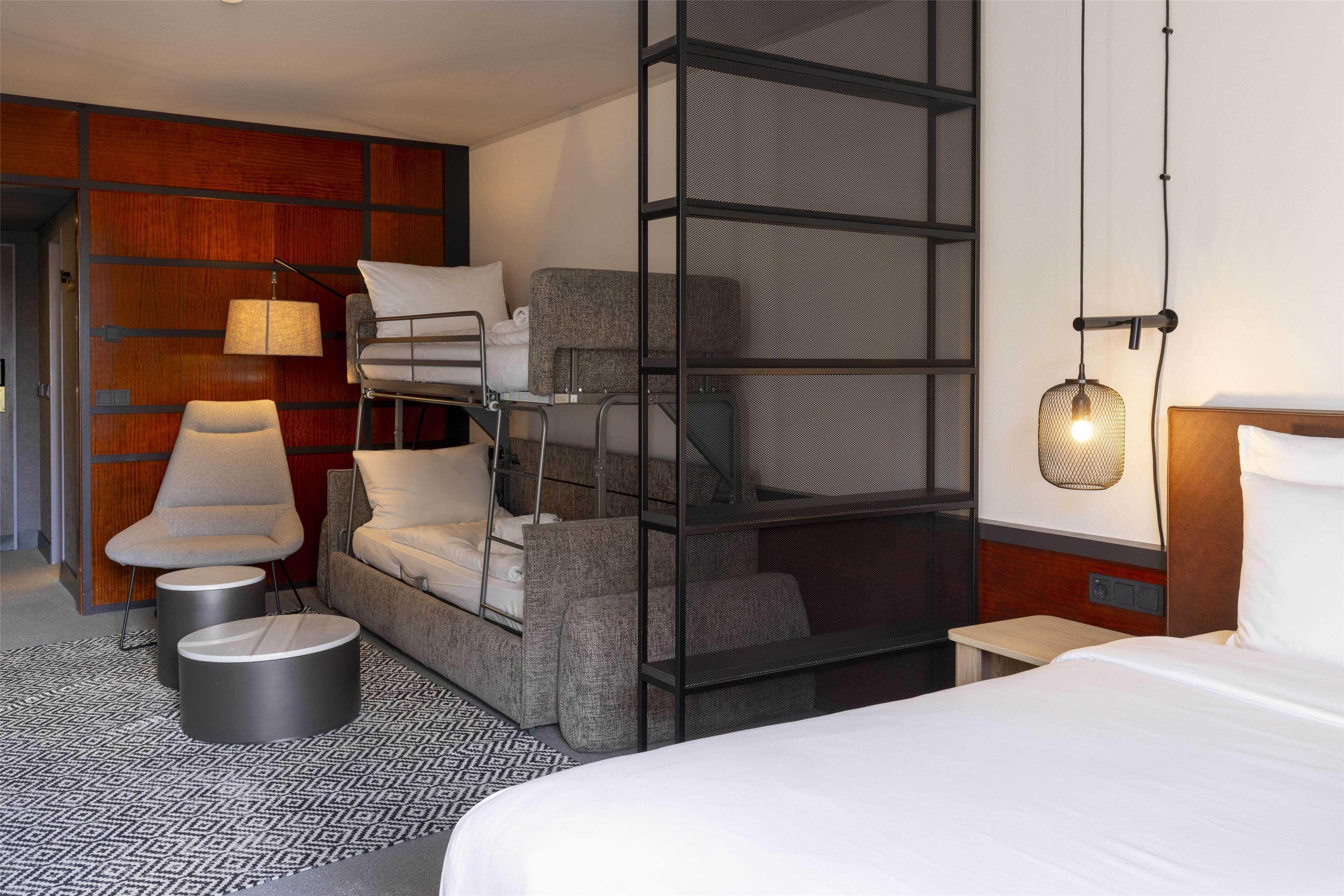 A modern hotel room with a bunk bed, a sofa, a chair, and a small table.
