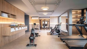 A modern gym with treadmills, stationary bikes, and a rowing machine. There are wooden shelves with towels and water bottles. - Scandic Nürnberg Central (Nuremberg)