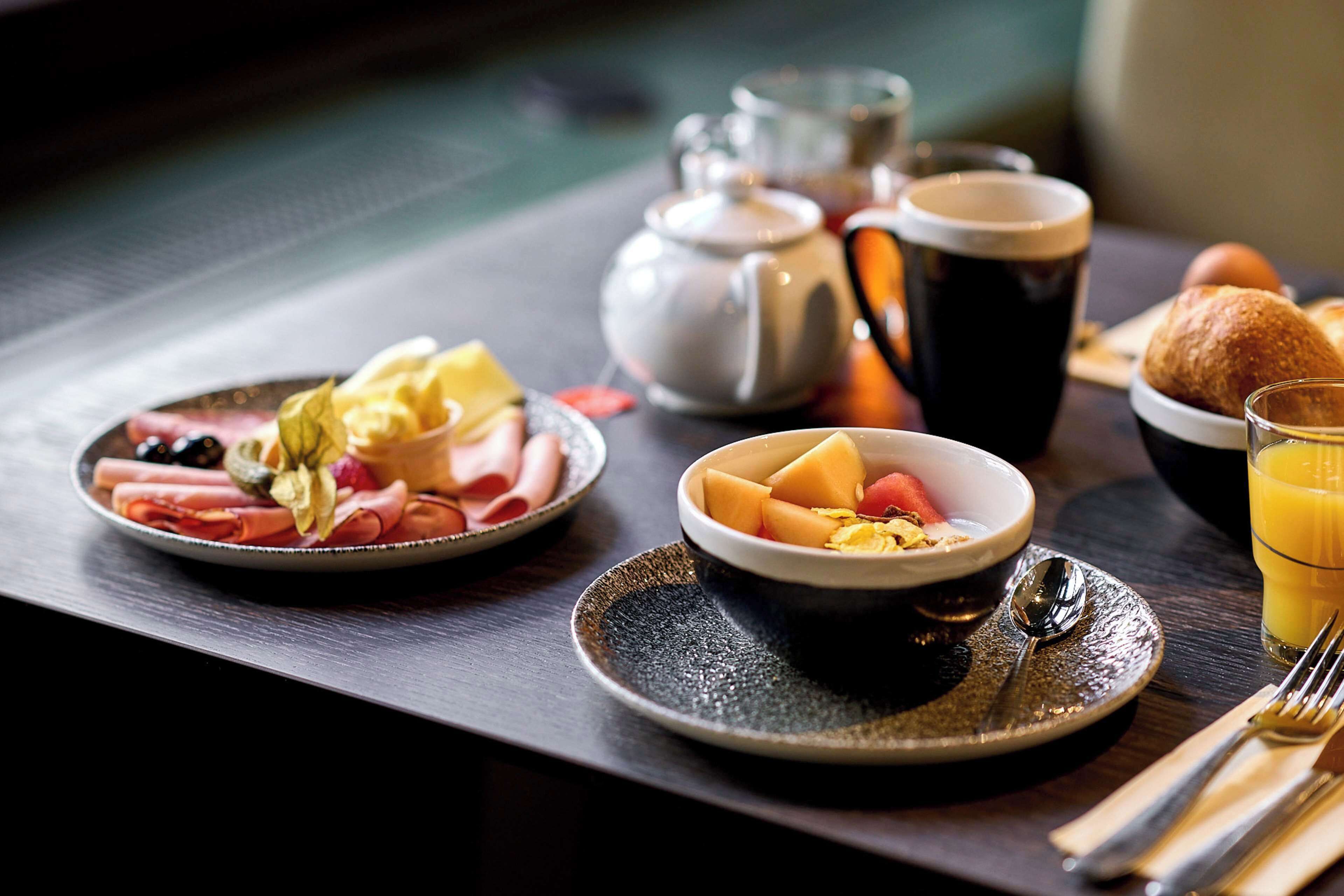 A breakfast setting with plates of food, a teapot, cups, and a glass of orange juice.