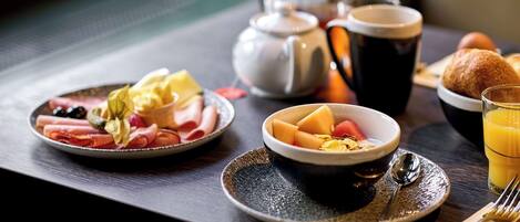 Une table mise pour le petit-déjeuner, avec des assiettes remplies de nourriture, une théière, des tasses et un verre de jus d’orange.