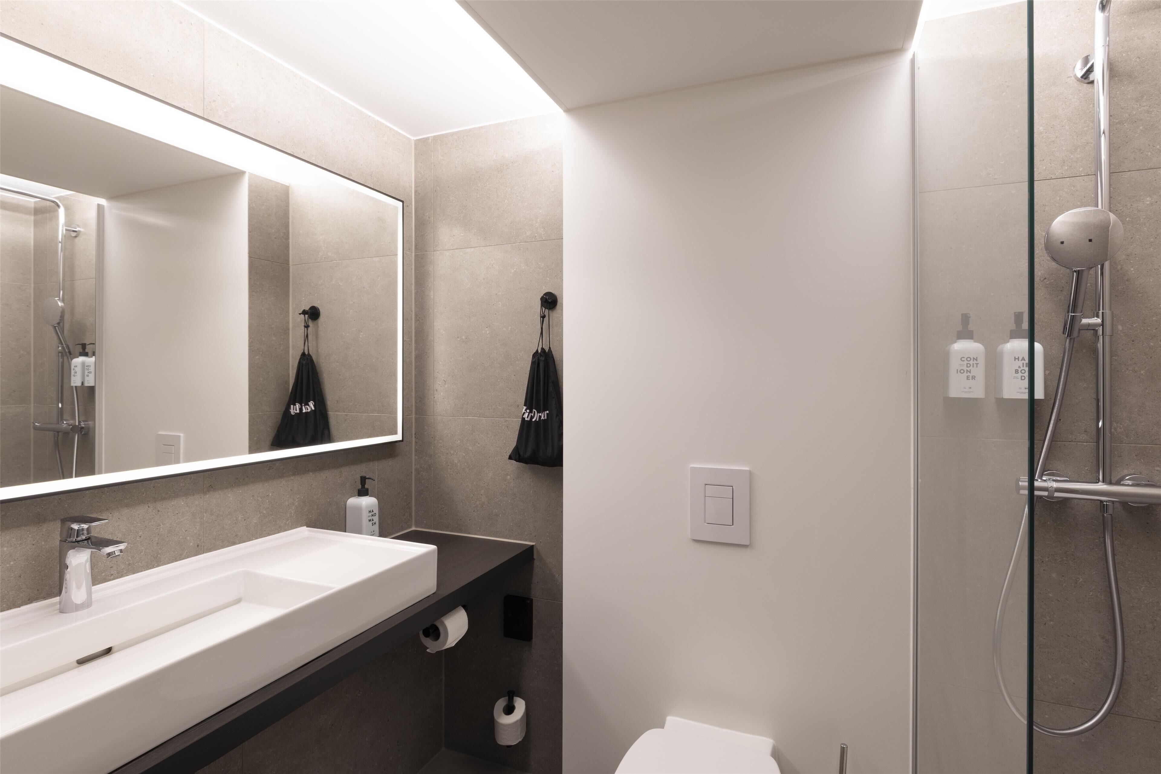 Un baño moderno con un espejo grande, un lavabo blanco, una ducha y un perchero para toallas.