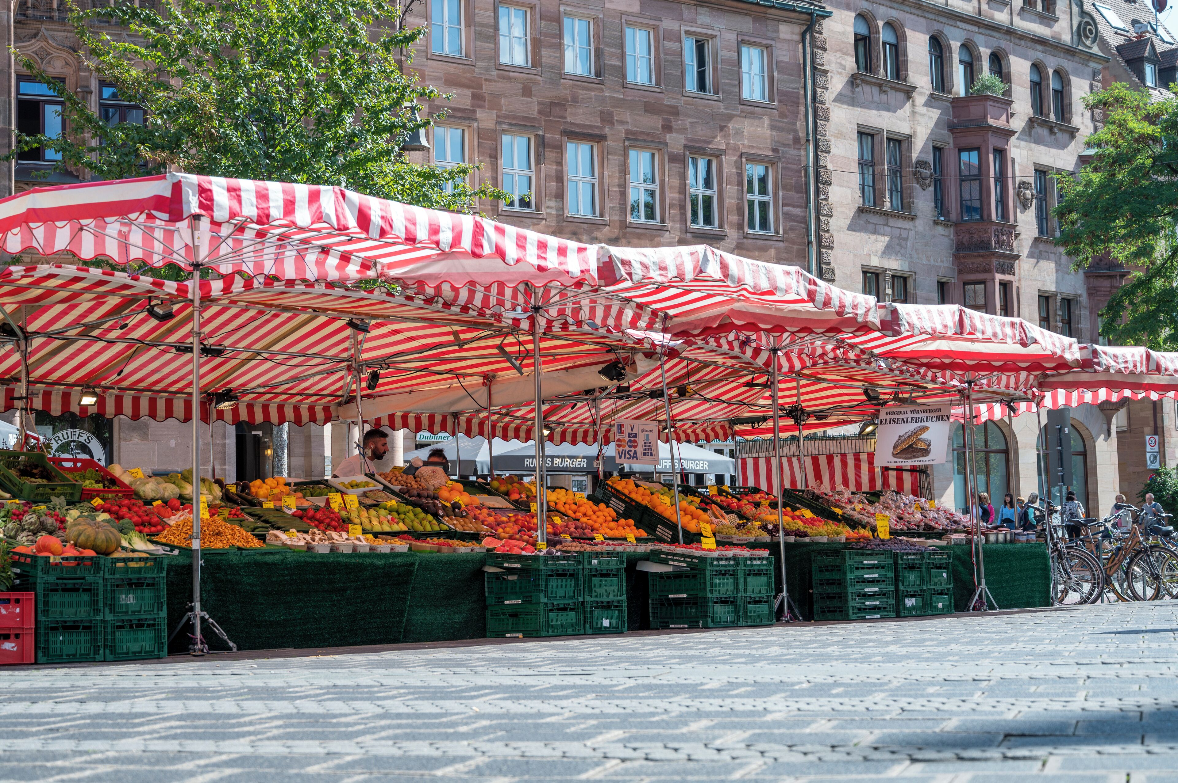 Un mercato con ombrelloni biancorossi, frutta e verdura in mostra e biciclette parcheggiate nelle vicinanze.