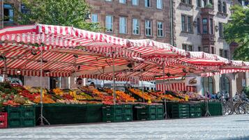 A market with red and white striped umbrellas, various fruits and vegetables on display, and bicycles parked nearby.