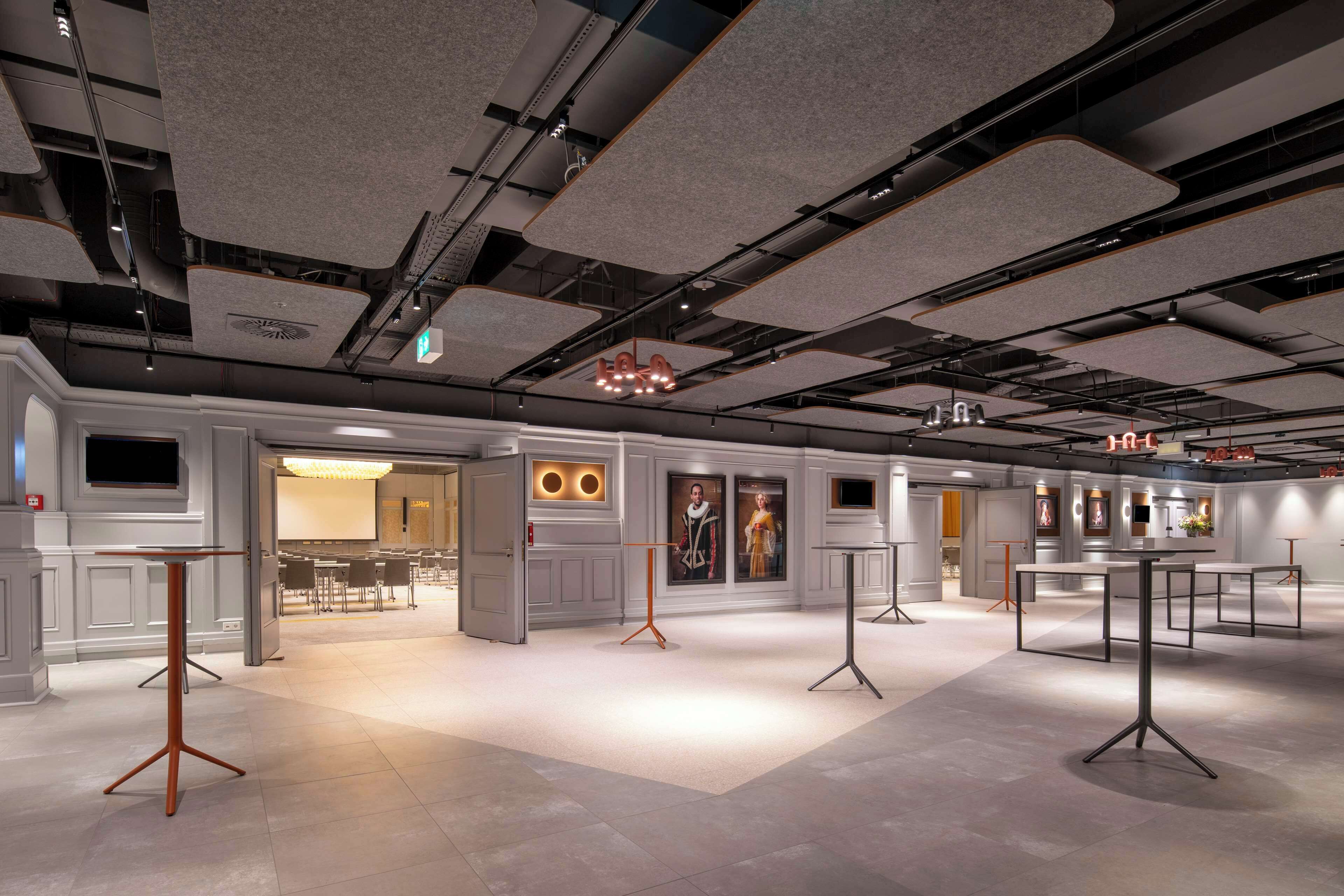 A spacious hotel lobby with modern furniture, a large chandelier, and a well-lit ceiling with exposed pipes.