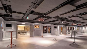 A spacious hotel lobby with modern furniture, a large chandelier, and a well-lit ceiling with exposed pipes.