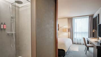 A hotel room with a shower, a bed, a desk, and a TV.