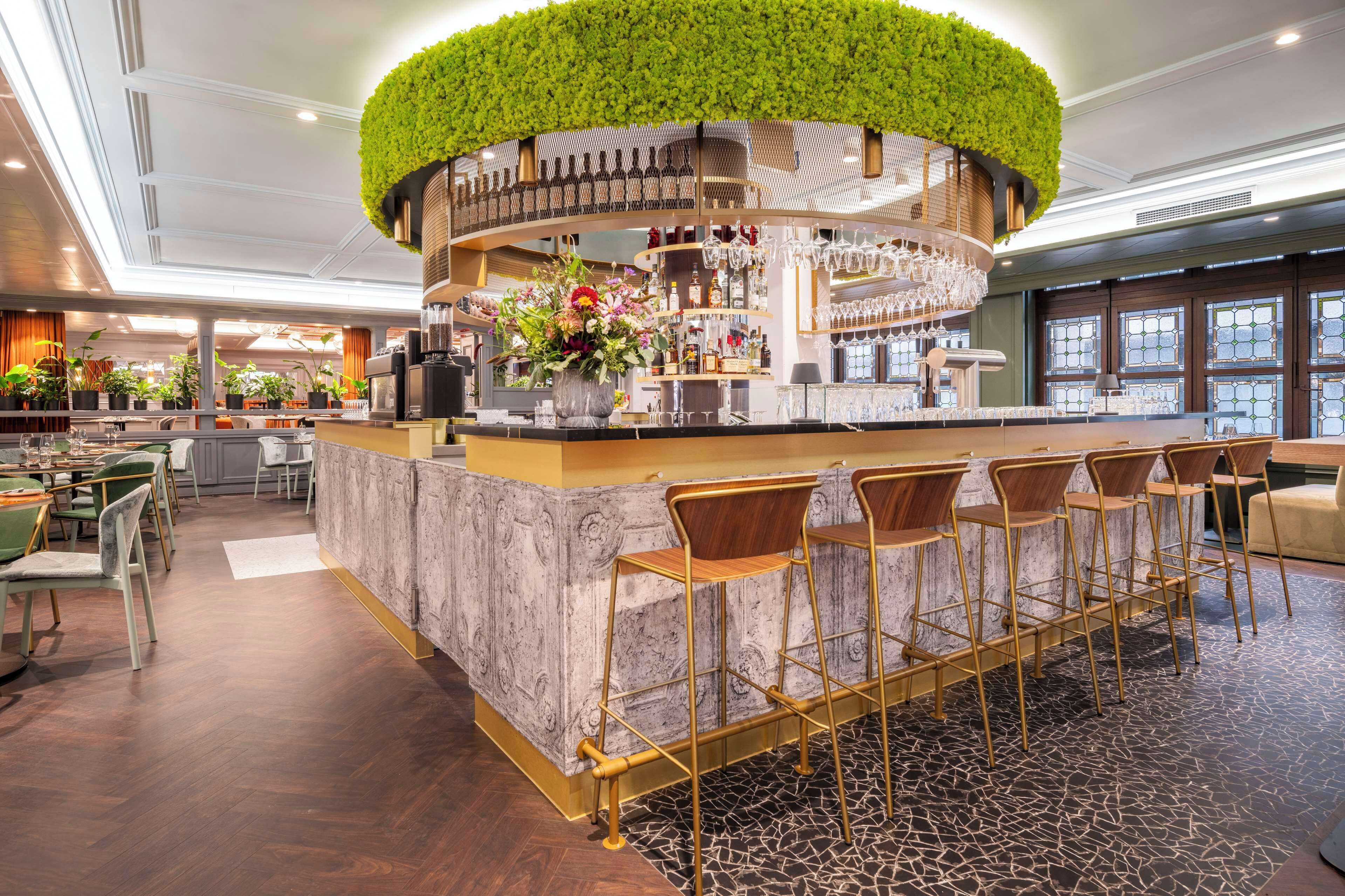 A bar area with a circular green plant top, bar stools, and a marble counter.