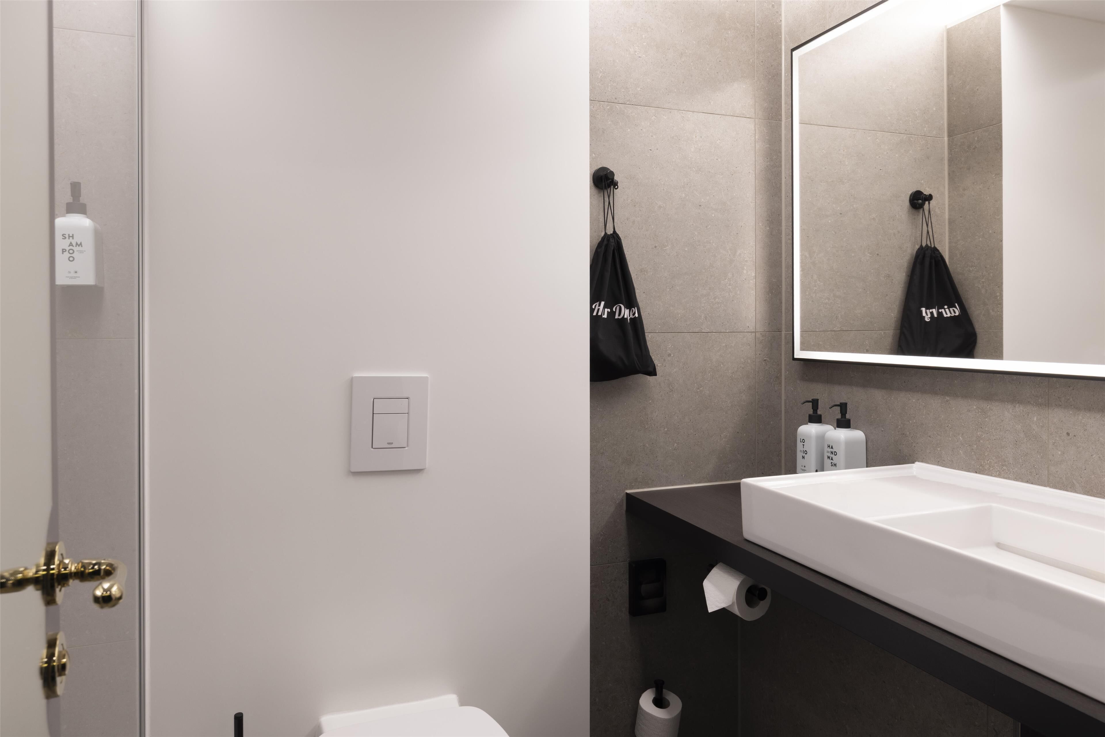 A modern bathroom with a white sink, a large mirror, and a towel hanging on a hook.