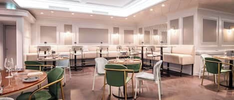 A modern dining area with round tables, green upholstered chairs, and a neutral color palette.