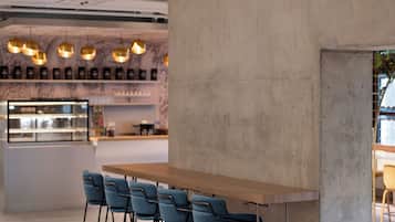 A modern bar area with a concrete accent wall, a long wooden bar, and blue bar stools.