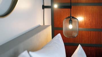Un lit bien fait, avec des oreillers blancs et une lampe suspendue au-dessus.