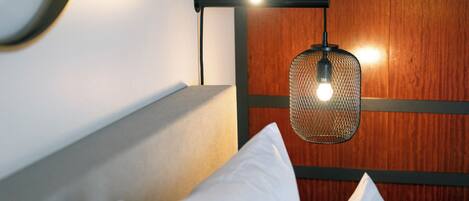 Un lit bien fait, avec des oreillers blancs et une lampe suspendue au-dessus.